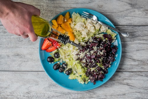 Olive oil being poured over blue plate of healthy foods and salad
