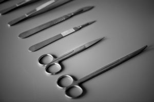 Scissors and scalpels used for eye bag removal laid out on a steel bench